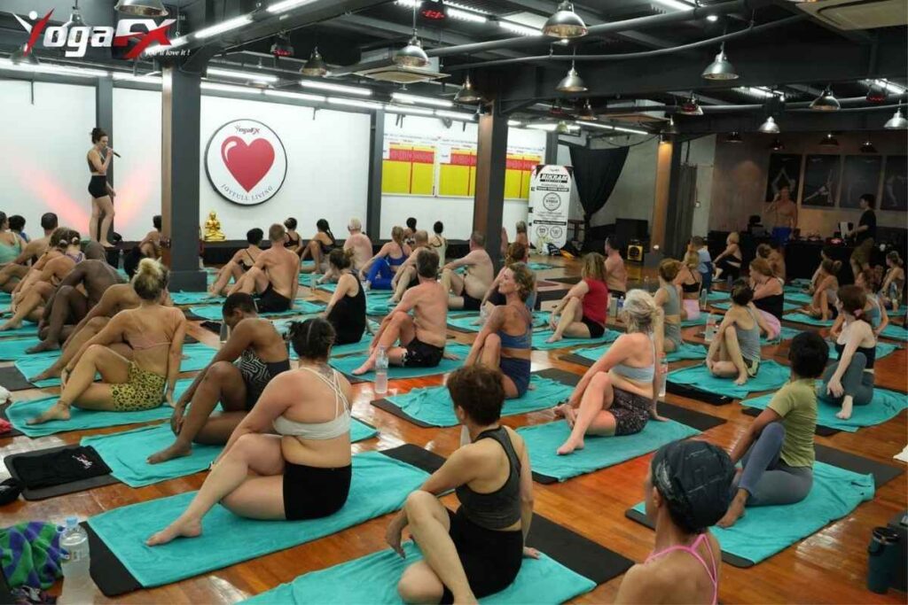 Full hot yoga class seated on mats at YogaFX studio listening to instructor before practice