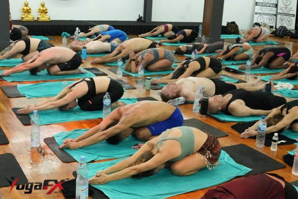 Hot yoga students stretching with towels and water bottles, showing what to bring to hot yoga class