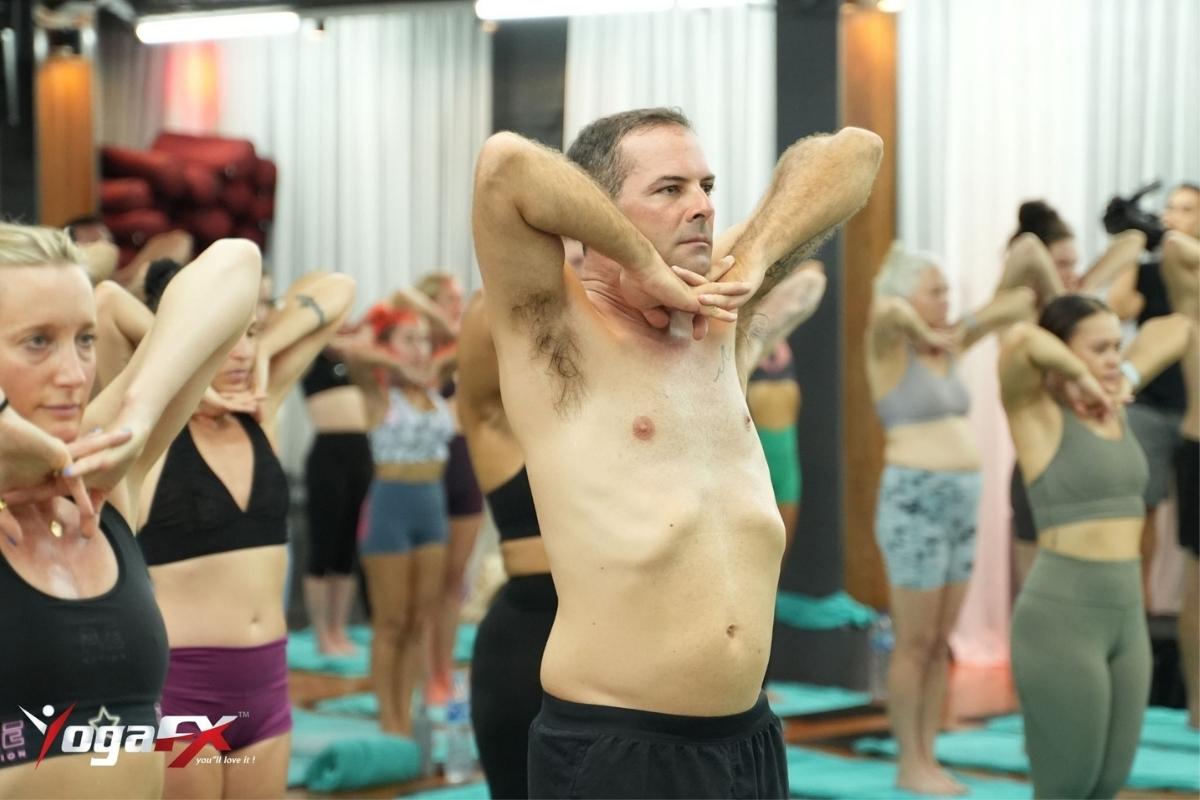 Man sweating through a standing posture in a Bikram-style hot yoga class, where larger bodies tend to store more heat