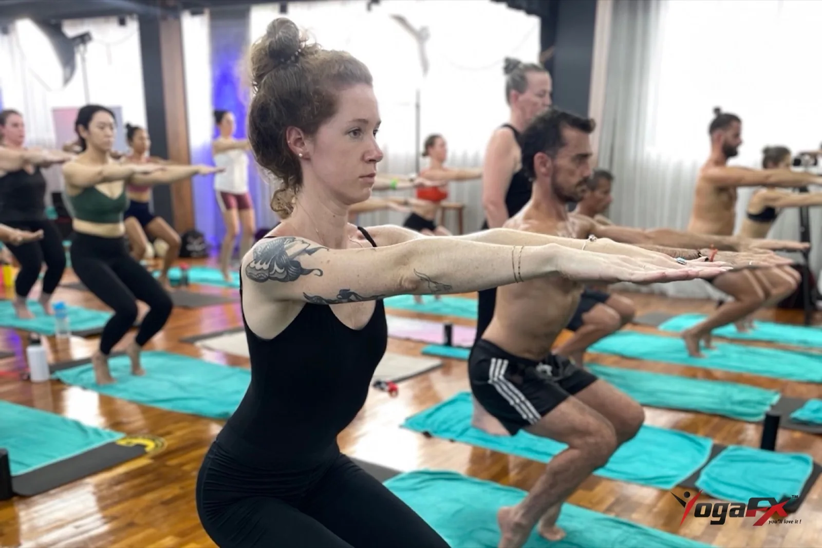 Group holding awkward pose with arms extended in a YogaFX hot room, building the leg strength used in yoga championship routines
