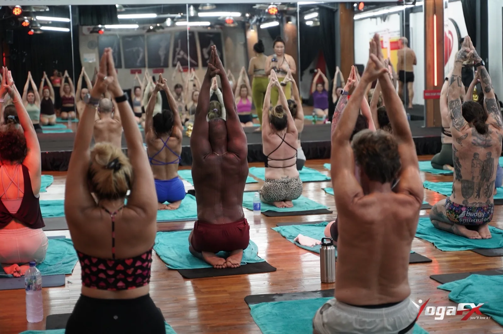 Trainees raise their hands overhead together in a hot 26&2 yoga teacher training class in Bali