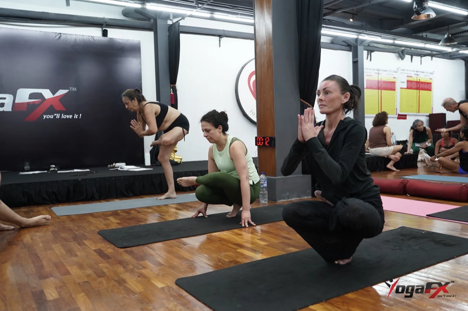 Trainees practise balance postures beside a countdown timer during teacher training, the same timed discipline used in competition